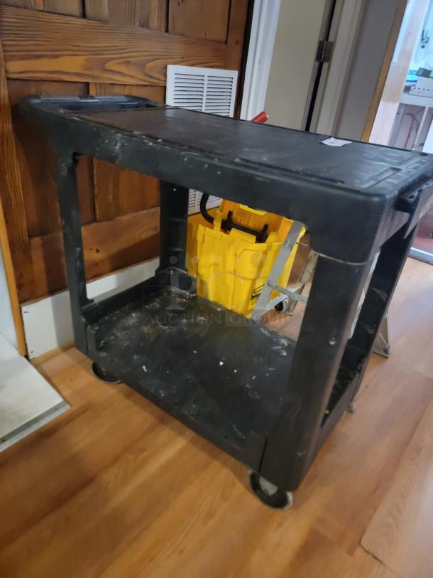 Commercial utility lot featuring a black rolling cart, yellow mop bucket, and metal step ladder, ideal for organization tasks.