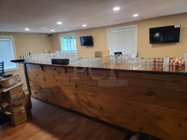 Custom 18-foot wooden bar with rustic finish, ideal for bars or events. Includes glassware, buyer disassembles.
