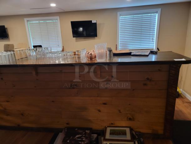 Custom 18-foot wooden bar with rustic finish, featuring a smooth top. Perfect for events or home use. Buyer disassembles and removes.