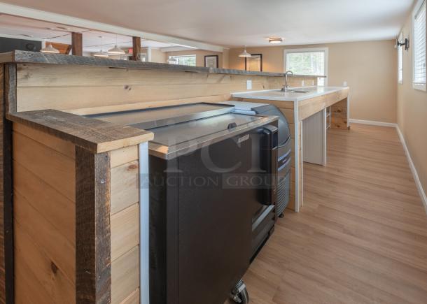 18-foot custom wooden bar with rustic finish, features a sink and under-counter space. Ideal for events or hospitality use.