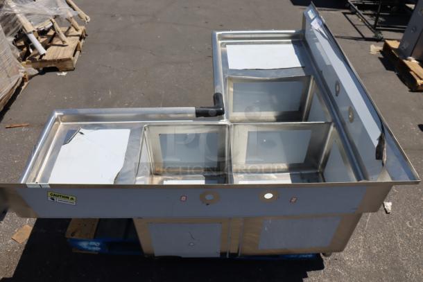 Brand new Regency 600S31620C 57" stainless steel commercial corner sink with three compartments, two drainboards, and visible dents.