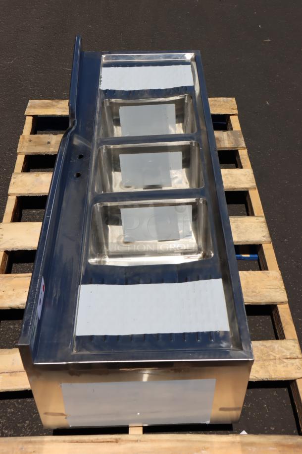 Brand new Regency 600B32160213 60" x 21" three-bowl underbar sink with two 13" drainboards, displayed on pallet.
