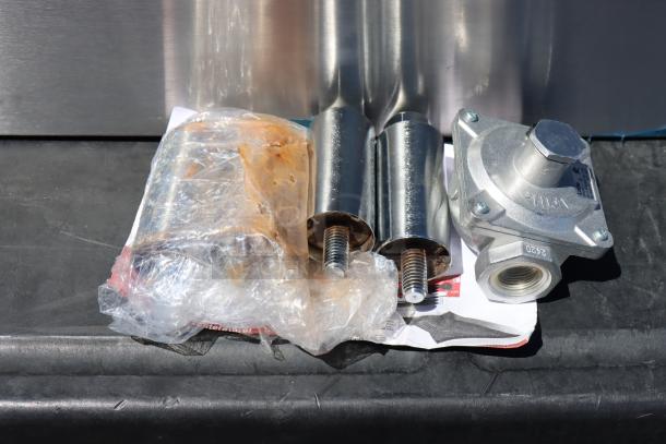 Avantco Chef Series 2 Burner Gas Range components, wrapped in plastic. Includes a metal gas regulator and parts. Model CAG-R-2-12.