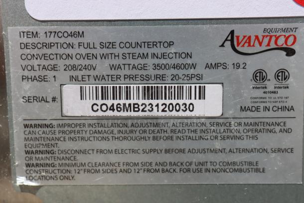Alt text: Close-up of label on Avantco CO-46M convection oven, serial CO46MB23120030, showing voltage, wattage, and safety warnings.