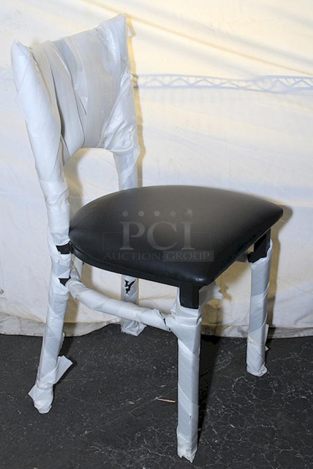 Brand new Lancaster Table & Seating chair, covered in protective wrapping, features black cushioned seat; part of a 20-chair set.