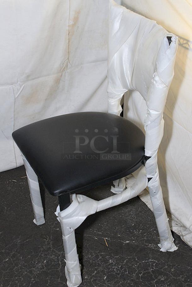 Brand new Lancaster Table & Seating chair wrapped in protective material, black seat cushion, wooden legs.