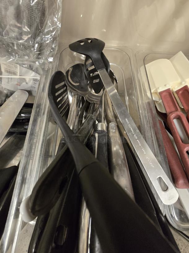 Assorted kitchen utensils including ladles, spoons, and spatulas in plastic bins. Mixed materials, good condition.