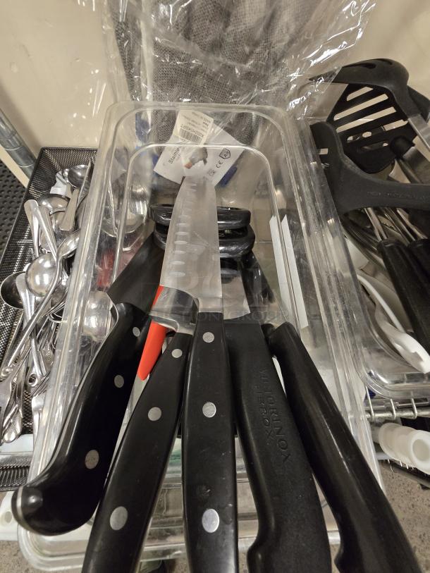 Box of 5 chef knives with black handles, including a Victorinox. Knives in plastic container, likely lightly used.
