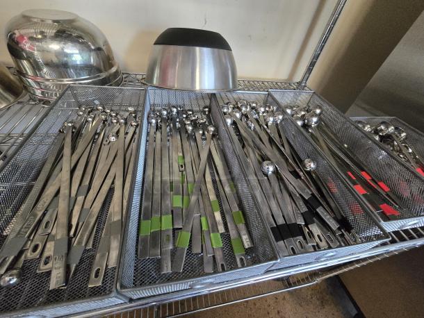 Stainless steel long-handled measuring spoons with red banding, organized in mesh trays; 12x your bid.
