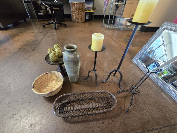 Assorted home decor items including a large vase, candles on metal stands, woven baskets, and decorative pineapples.