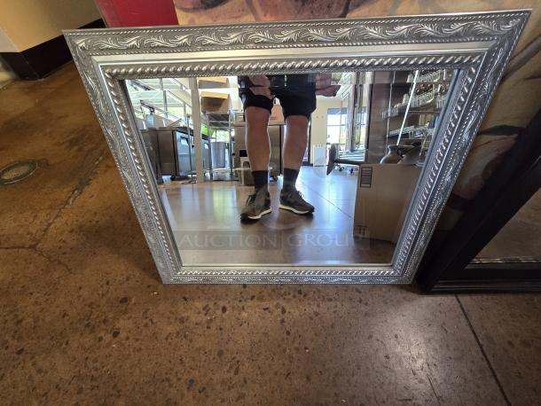 Medium sized mirror with ornate silver frame, reflecting a room interior. Frame features intricate leaf patterns.