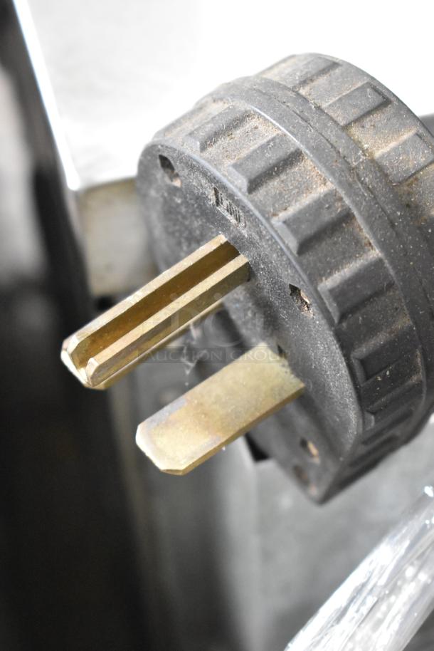 Close-up of a black and brass power plug for a commercial appliance, showing wear and surface dust.