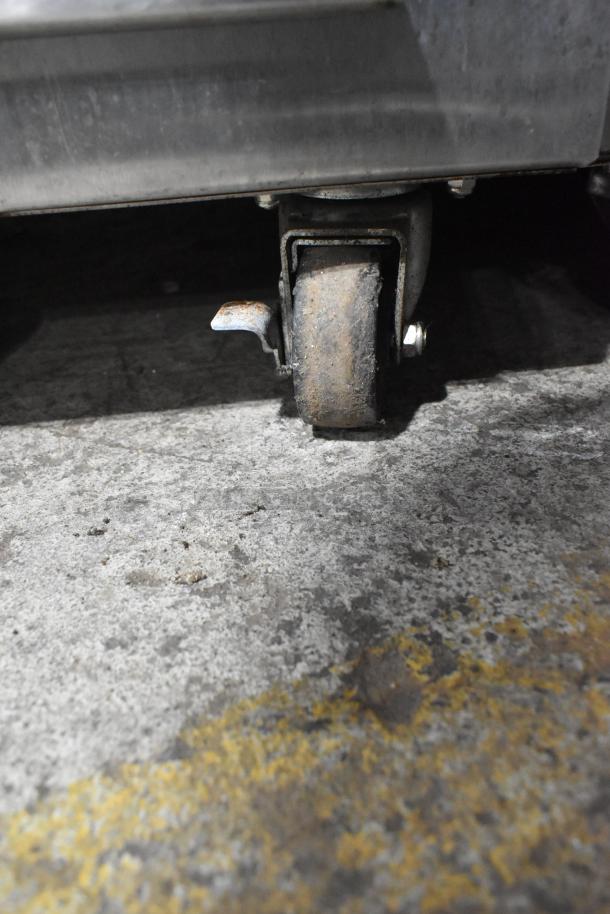 Rusted caster wheel of Nu Vu SUB-123P stainless steel commercial oven proofer. Seen on concrete floor.