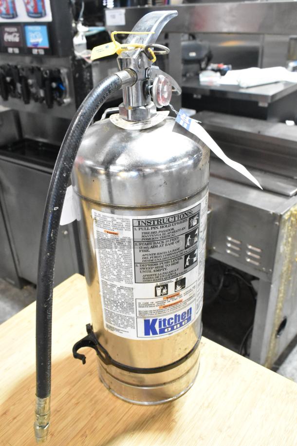 Brand new Kitchen One wet chemical fire extinguisher, stainless steel, includes hose and instruction label, slight dents.