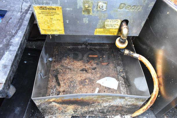 Dean stainless steel commercial fryer oil filtration system showing wear and residue. Caution and warning labels visible.