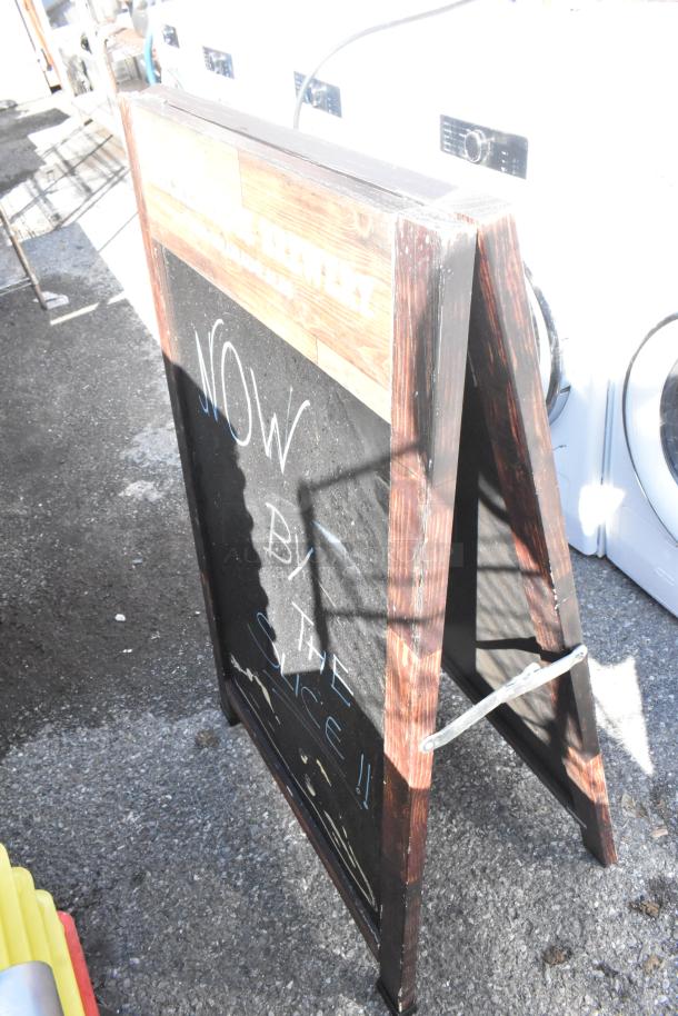 Wood pattern A-frame sidewalk sign, dark finish, handwritten chalk text, sturdy design, visible wear, ideal for advertising.
