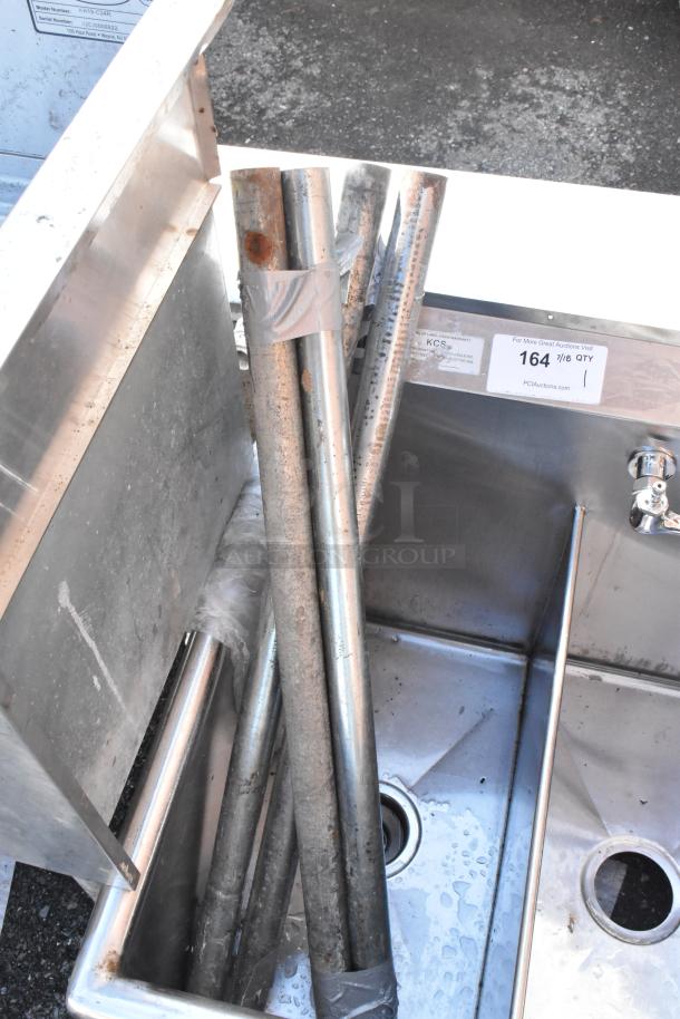 Stainless steel 3-bay sink with faucet and handles. Visible pipes, minor rust, and auction label. Used condition.