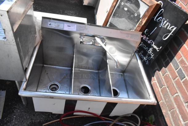 Stainless steel 3 bay sink with faucet, handles, and visible auction tag. Shows signs of light use.