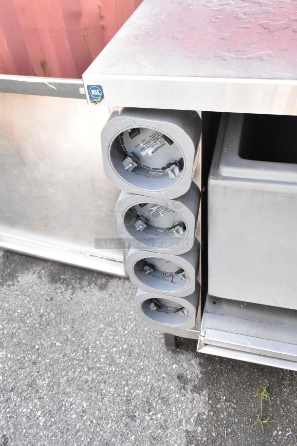 Stainless steel counter with four built-in cup dispensers. Features an NSF label. Good condition with some surface wear.