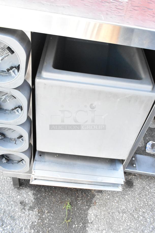 Stainless steel counter with four built-in cup dispensers on the side, in good condition. Medium-sized storage bin below.