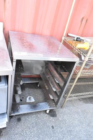 Stainless steel pan transport rack on commercial casters, shows some surface wear, features racks for multiple pans.