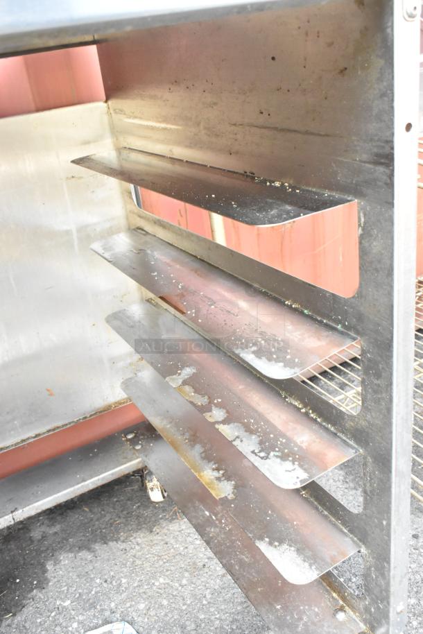 Stainless steel pan transport rack with visible wear on commercial casters, featuring multiple shelves.