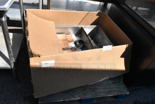 Cardboard box containing a metal unit with perforated sides. Visible labels and barcodes on the box indicate product details.