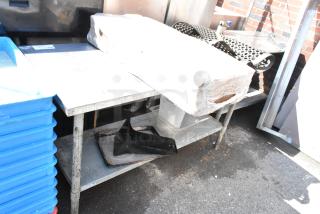 Stainless steel table with metal under shelf, holding blue bins, anti-fatigue mat, wrapped item, and plastic container.
