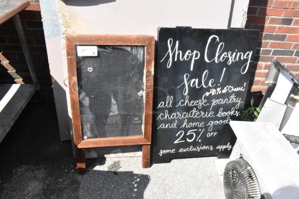 Two A-frame sidewalk signs; one with rustic wooden frame, another with hand-painted sale text. Signs in fair condition.