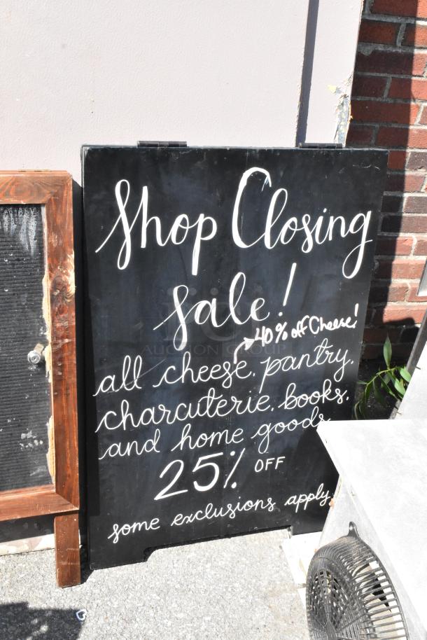 A-frame sidewalk signs, black with white text, advertising a shop closing sale. Includes discounts and product categories.