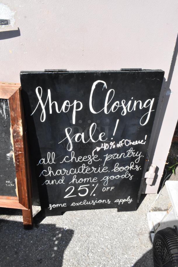 Two black A-frame sidewalk signs with “Shop Closing Sale” and discount details in white script. Signs show minor wear.