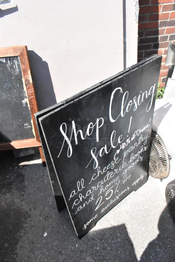 Two A-frame sidewalk signs, black with white text, advertising a shop closing sale. Condition appears used.