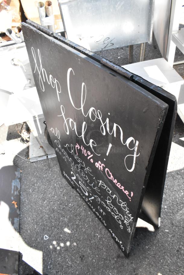 Two black sidewalk A-frame signs with white handwritten text, advertising a shop closing sale. Signs appear in fair condition.