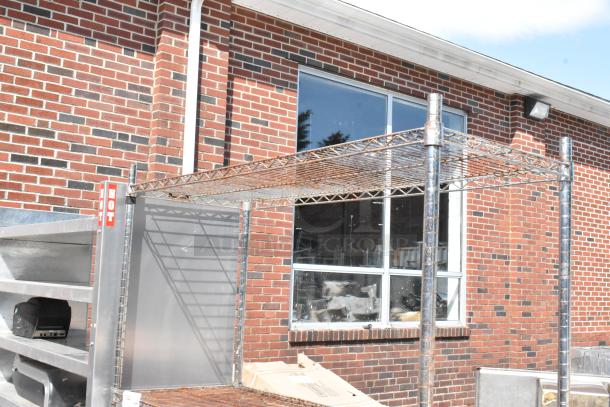 Chrome finish 4-tier wire shelving unit outside a brick building; buyer must dismantle. Consider freight charges.