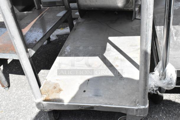 Metal two-tier cart with commercial casters, showing signs of wear; used industrial storage or transport solution.