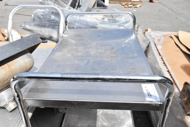 Stainless steel 2-tier cart on commercial casters, has protective plastic wrap, minor scratches visible, ideal for industrial use.