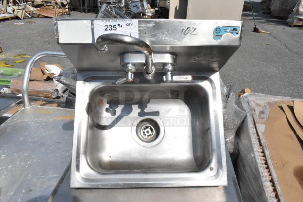 Stainless steel single bay wall mount sink with dual faucet and handles, visible NSF certification, lightly worn condition.