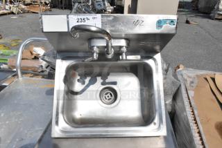 Stainless steel single bay wall mount sink with dual faucet and handles, visible NSF certification, lightly worn condition.