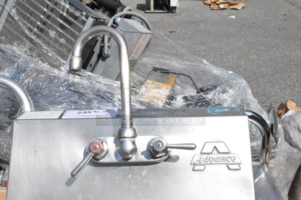 Stainless steel single bay wall mount sink with faucet, handles, and "Advance" branding, in used condition.