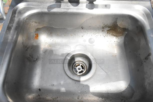 Stainless steel single bay wall mount sink with faucet and handles, showing signs of wear and some rust spots.