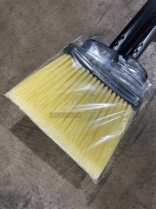 New commercial floor broom with black grip handle, yellow bristles, wrapped in plastic packaging, shown on concrete floor.