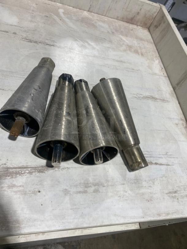 Set of four stainless steel adjustable legs for Victory commercial freezer, with visible screws, in used condition on wooden surface.