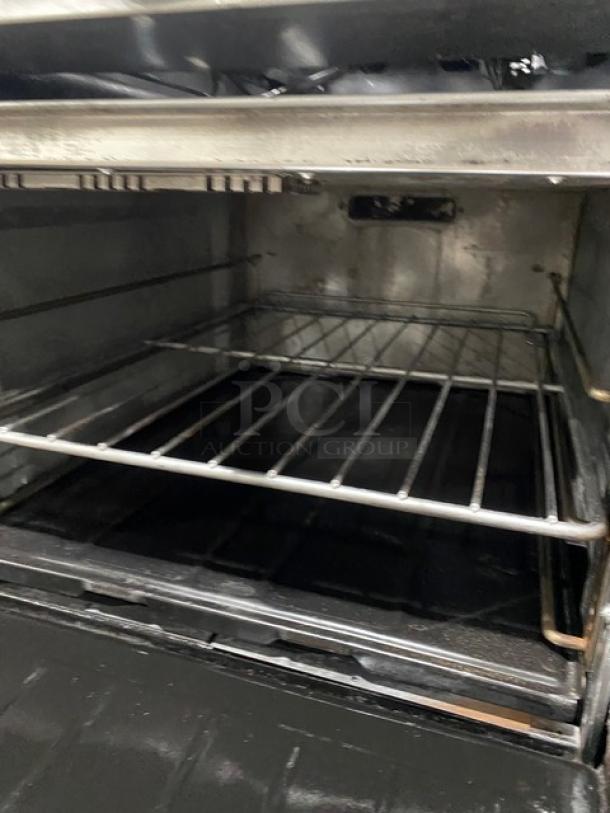 U.S. Range stainless steel 8 burner stove with double oven, backsplash, overhead salamander shelf, and wired racks shown.