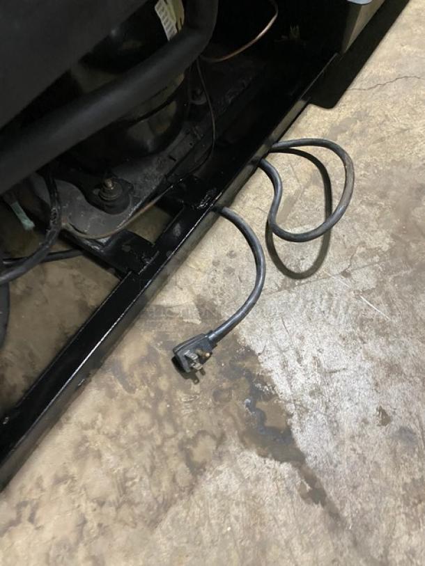 Close-up of the plug and base of a True Commercial Refrigerator Model GDM-41SL-54, showing grounding wire and part of the compressor area.