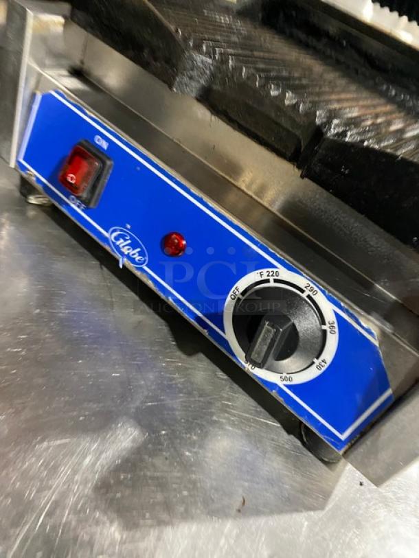 Globe stainless steel electric panini grill with grooved top and bottom grates. Features thermostatic control, 120V, on legs.