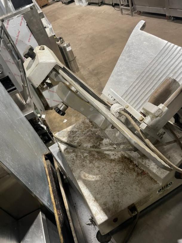 Univex Duro Series commercial electric deli meat slicer on legs. Features adjustable blade, sturdy metal construction, and countertop design. Visible wear from use.