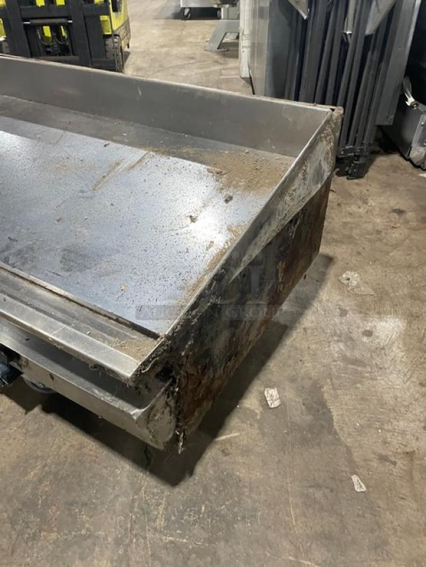 Commercial stainless steel natural gas countertop flat griddle with back and side splash, on legs, shows wear.