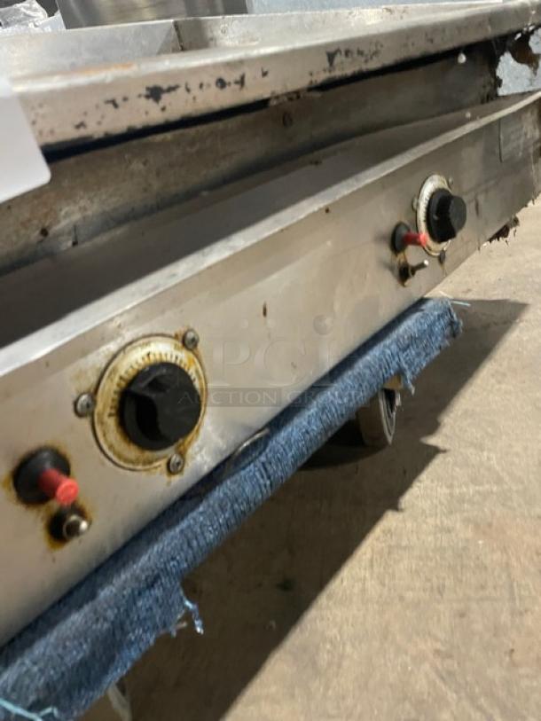 Commercial stainless steel countertop flat griddle with natural gas power, back and side splash, on legs. Worn condition.