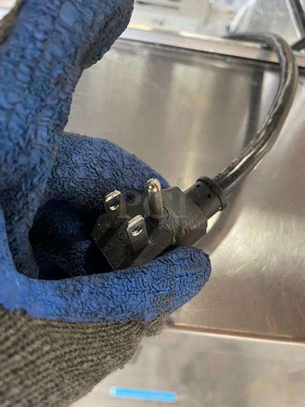 Close-up of Turbo Air prep table's power cord, showing a three-prong plug, held by a hand in a blue glove.