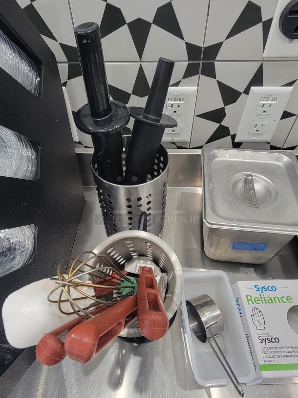 Commercial kitchen equipment, including utensils, whisks, spatulas, and metal scoops in good, used condition. Sysco Reliance box visible.